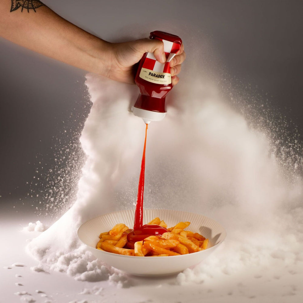 Une main verse la sauce piquante Paradox dans une assiette de frites avec de la vapeur en arrière-plan.