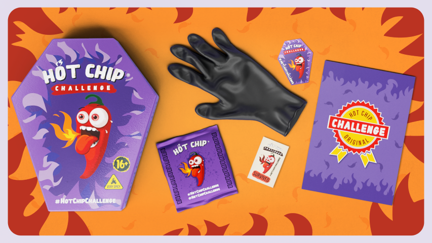 Le pack HOT-CHIP Challenge présenté avec un gant noir, sachets de chips piquantes, et boite de sauce piquante.