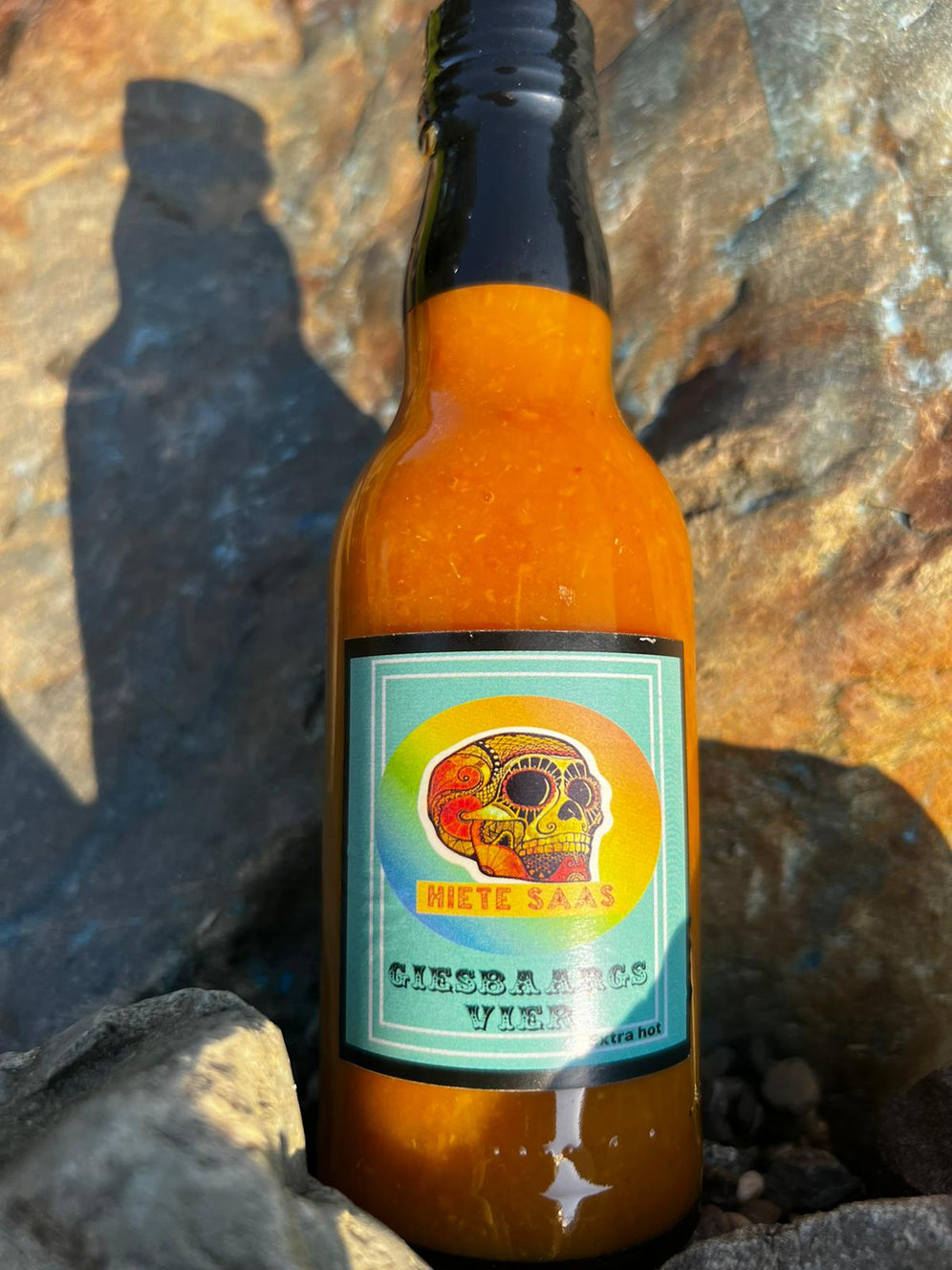 Bouteille de sauce Giesbaargs Vier avec Carolina Reaper rouge et jaune posée sur des rochers, sauce piquante barbecue, 200ml.